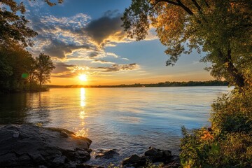 Golden Sunset Over a Tranquil River with Trees and Rocks in the Foreground