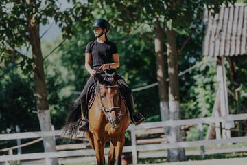 A young woman is riding a horse in a lush outdoor equestrian environment, showcasing skill and...