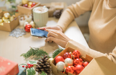 Happy young woman using smartphone mobile addict spending time in front of Christmas tree at home celebrating new year and Christmas