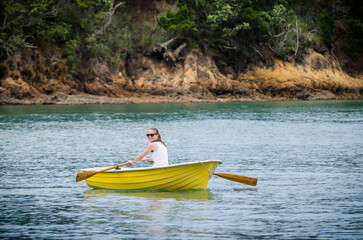 Young woman rowing a small yellow boat on calm water