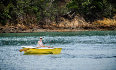 Young woman rowing a small yellow boat on calm water