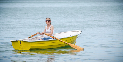 Young woman rowing a small yellow boat on calm water © Nathan McClunie