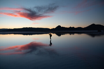 Woman silhouette taking a picture at the Utah Salt Flats with reflection at sunset