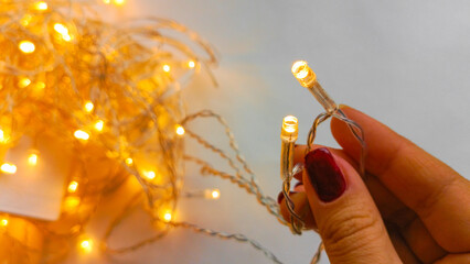 A woman's hand holds two garland diodes in close-up. Yellow garland lights on a white background....