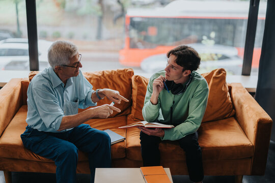 An elderly mentor providing guidance to a young student seated on a cozy sofa. The discussion embodies wisdom sharing and attentive listening in a quiet study environment.