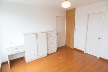 habitacion de departamento con closet empotrado o incorporado, con acabdos en melamina en habitacion moderna con piso de madera y paredes blancas