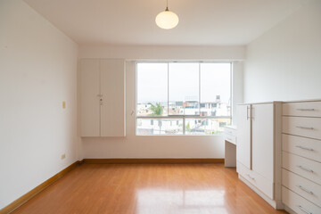 habitacion vacia de departamento con ventana hacia la calle paredes blancas y  piso de melamina color madera