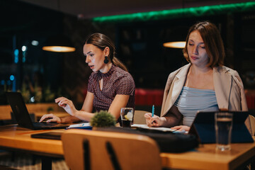 A diverse group of business professionals working late, analyzing data on laptops. The scene highlights teamwork, focus, and strategic planning in a modern office environment.