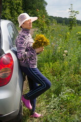 beautiful mature women standing in a field near a car with a bouquet of medicinal plant St. John's...