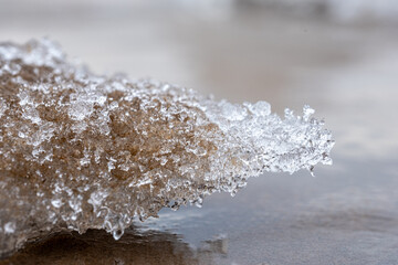 Close-up view of frozen water droplets on a sandy surface in winter, showcasing intricate ice formations on a chilly morning