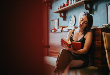 A woman sits comfortably in a modern cafe, engrossed in reading a book. The atmosphere is warm and...