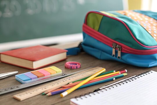 Schreibwaren und Schulmaterial vor Tafel mit farbigem Rucksack