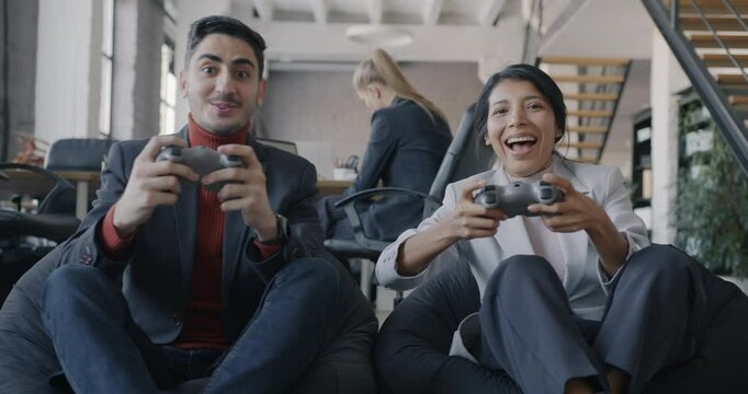 Portrait of joyful Middle Eastern businesspeople man and woman playing video game with wireless controllers having fun in work break in office. Gaming and workplace concept.