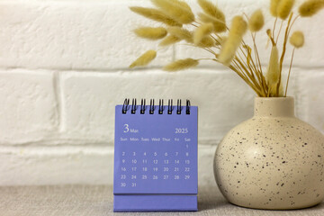 Desk calendar for March 2025 and dried flowers on the table.