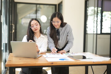 Happy Asian business people working together using laptop and tablet in office.