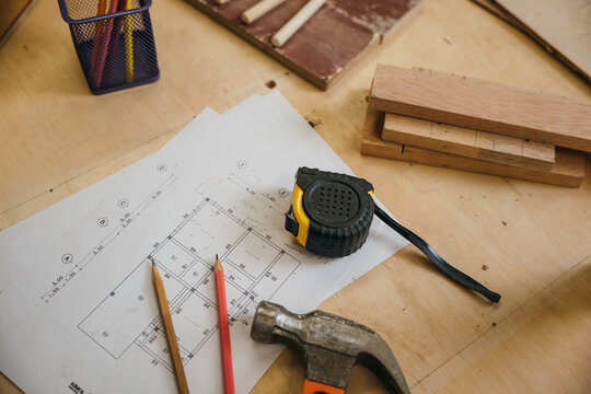 Wooden surface with tape measure, hammer, pencils, and blueprint. Renovation tools and apartment plans laid out, perfect for home improvement, construction, and renovation concepts.