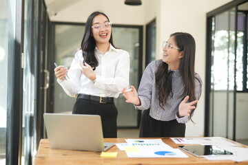 Happy Asian business people working together using laptop and tablet in office.