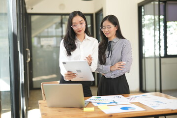 Happy Asian business people working together using laptop and tablet in office.
