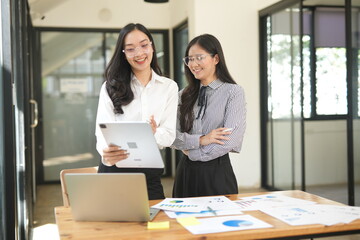 Happy Asian business people working together using laptop and tablet in office.