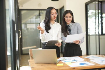 Happy Asian business people working together using laptop and tablet in office.