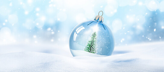 Weihnachtskugel aus Glas vor verschneiter Landschaft im Hintergrund