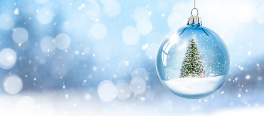 Weihnachtskugel aus Glas vor verschneiter Landschaft im Hintergrund