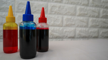 Close-up photo of red, blue, yellow, and black ink in transparent plastic bottles with a white background. Perfect for printing industry themes, office supplies, or creative design projects.