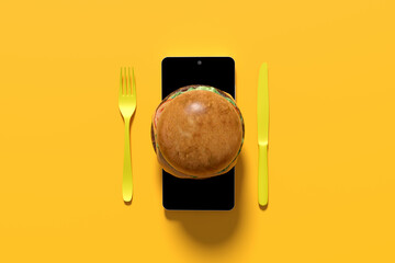 Burger displayed on smartphone screen with cutlery on yellow background