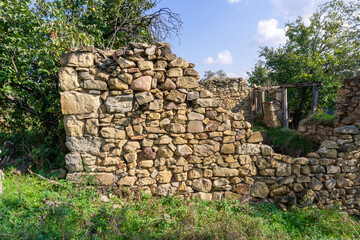 An old ruined wall made of large stones illuminated by sunlight. Grass and trees around