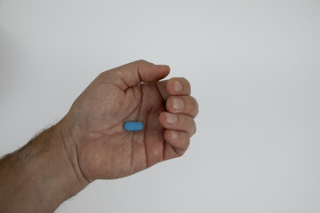 Slightly closed caucasian male hand with a blue pill in the palm of the hand. Hand against white background. 