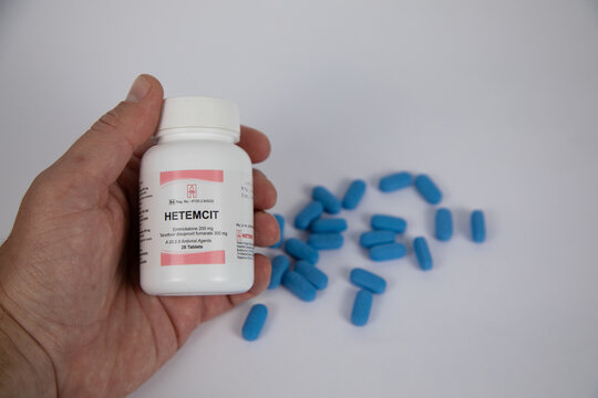 Bottle of Hetemcit pre-exposure prophylaxis pills in a caucasian hand.  In the background blue pills out of focus against a white background.