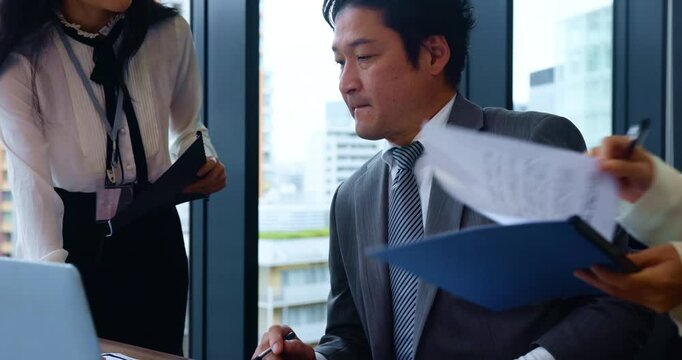 Japanese, businessman and multitasking for ideas, concentration and documents at office. Male person, thinking and colleagues for time management, busy and technology with paperwork in finance agency