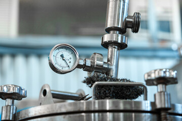 A pressure gauge on a stainless steel tank in an industrial setting displays the pressure reading