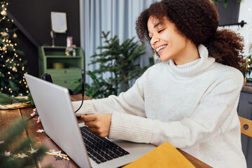 African woman in sweater is sitting at table with laptop and microphone