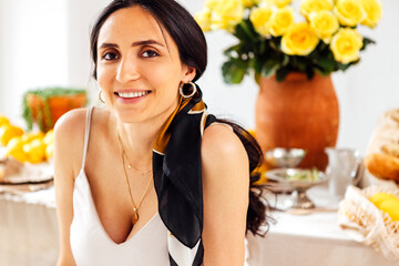 A close-up of a young woman with a scarf in her hair. A charming brunette in a white dress is smiling in the kitchen at home. Italian cozy interior style.