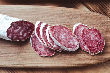 slices of traditional Spanish sausage salami fuet or dry sausage, covered with fermented mold on a wooden table.