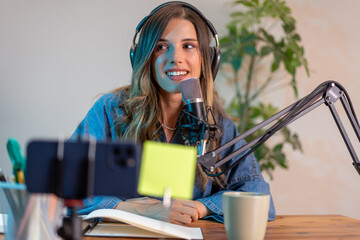 Young female content creator recording podcast using professional microphone and digital devices in...