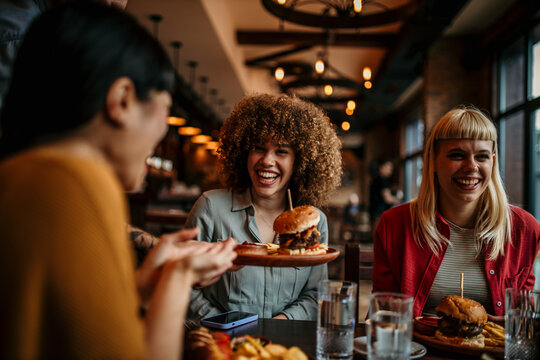Young happy people having lunch together. An unrecognizable man passing burgers to his female friend. - Powered by Adobe