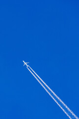 Aeroplane flying on a clear blue sky with white vapor trails