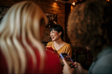 Photo of cheerful friends during a dinner party in an indoors bistro, having fun while taking photos and selfies