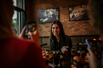 Photo of cheerful friends during a dinner party in an indoors bistro, having fun while taking photos and selfies