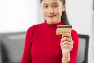 A cute businesswoman sits at her office desk, smiling happily while holding a yellow credit card....