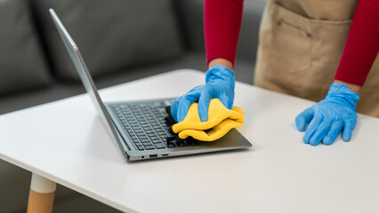 A young woman cleans her desk at home, using a disinfectant spray and a wipe. She ensures a hygienic and organized workspace, emphasizing cleanliness and personal health in her routine