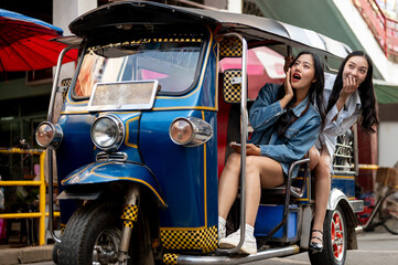 Two excited Asian girls enjoy a ride in a tuk-tuk in Thailand, amazed by the stunning views.