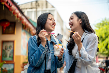 Two joyful Asian female friends explore the city in Chiang Mai, Thailand, enjoying ice cream.