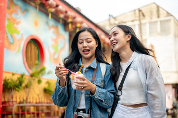 Two joyful Asian female friends explore the city in Chiang Mai, Thailand, enjoying ice cream.