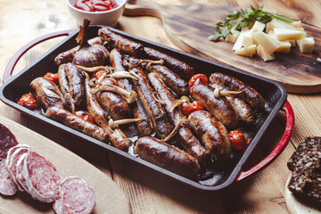 Grill pan with delicious homemade chicken, beef and pork sausages, with mushrooms and tomatoes on a wooden table with ketchup, bread and cheese.