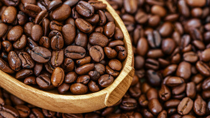 Roasted coffee beans in a wooden spoon on a coffee background. Close-up of roasted coffee beans in a wooden spoon on a background of scattered coffee beans, emphasizing natural texture and rich aroma.