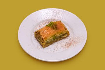 Close up view of piece of baklava with pistachio on white plate. Turkish dessert baklava plate on yellow background.