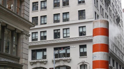Steam vapor vented on New York City street, orange vapour tube stack. Hot smoke from pipe. Con Edison's Steam Operations system, 5 Fifth avenue, Manhattan Midtown architecture.